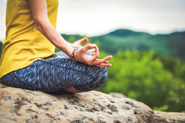 woman meditating in lotus pose on a rock in summer