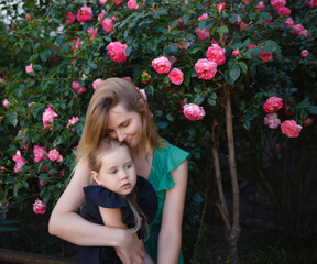 mom hugs her little daughter against the background of a rose bush