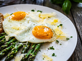 Tasty breakfast. Sunny side up eggs with green asparagus and parmesan served on black plate on wooden table
