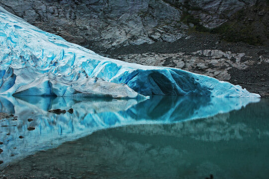 the blue Briksdal glasier, licking and caressing the sea at its end and doubling reflected in the sea water,  Oban, Norway