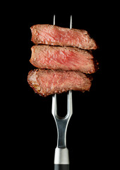 slice of steak on fork at black background