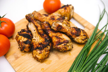 Fried chicken legs lie on a wooden board. Chicken shish kebab with a side dish of vegetables and green onions.