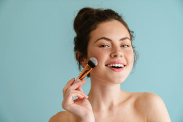 Half-naked brunette woman smiling while using cosmetic brush
