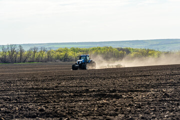 A blue tractor works on a field on a spring morning.