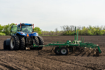 Obraz premium A blue tractor with seedbed cultivator works on a field on a spring morning.