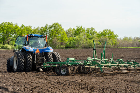 A blue tractor with seedbed cultivator works on a field on a spring morning.
