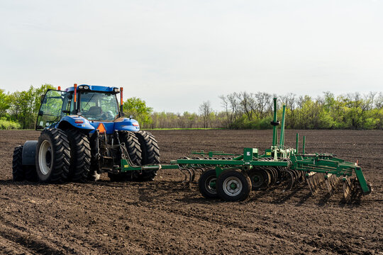 A blue tractor with seedbed cultivator works on a field on a spring morning.