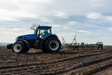 Fototapeta premium A tractor with seedbed cultivator ploughs field on morning.