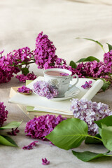Obraz na płótnie Canvas Romantic background with cup of tea ,lilac flowers and open book over white table