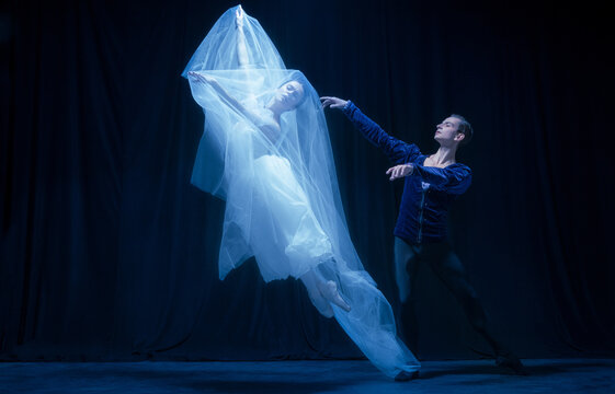 Young woman in wedding dress and man, two ballet dancers in art performance dancing isolated over dark background.