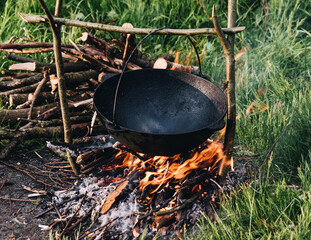 An empty cauldron warms up on a fire in the forest before cooking.
