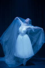 Young graceful balerina in image of ghost bride in art performance isolated on dark background in neon light. © Lustre Art Group 