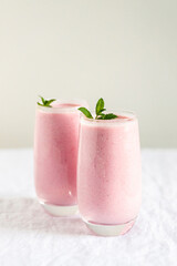 Two glasses of strawberry milkshake with mint garnish on table.