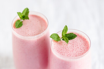 Close up of two glasses of strawberry milkshake with mint garnish.