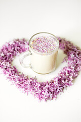 Lilac flowers laid out in the shape of a heart and a cup of hot morning coffee in a glass cup on a white background. Copy space for text. Concept of holidays and good morning wishes.