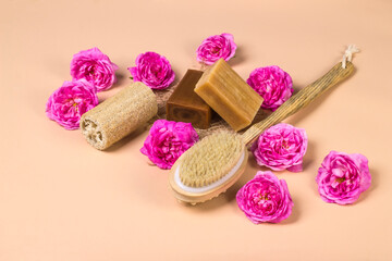 Fototapeta na wymiar Natural soap, loofah loofah and massage brush on a beige background with roses. Natural organic cosmetics for face and body. Skin care concept
