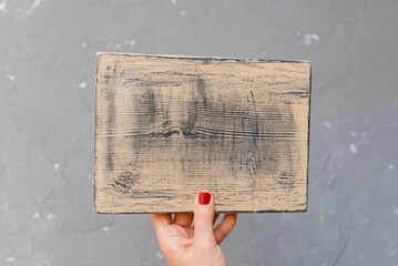 A female hand holds an empty wooden plaque. View from above. Close-up. Flat lay.