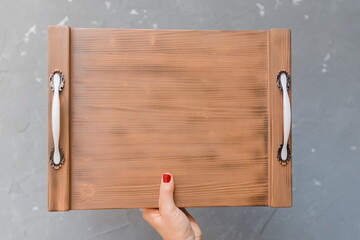 A female hand holds a wooden tray with handles. View from above. Close-up. Flat lay.