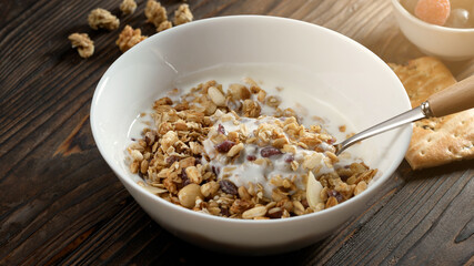 Homemade muesli cereals breakfast with white plain yogurt, dry nuts, in small bowl on rustic wooden background. Healthy granola, food clean eating, vegan diet, allergy-friendly weight loosing concept