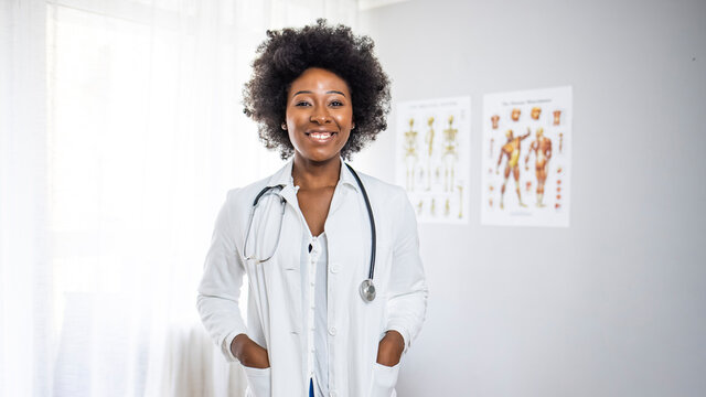 Portrait of beautiful smiling female african american doctor standing in medical office. Health care concept, medical insurance, copy space. Smiling female doctor with lab coat