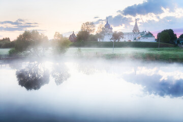 Suzdal town in Russia. Beautiful summer landscape at foggy sunrise. Nativity Cathedral and trees are reflected in the river.