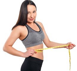 A slender woman measures her waist with a measuring tape. n a white background.