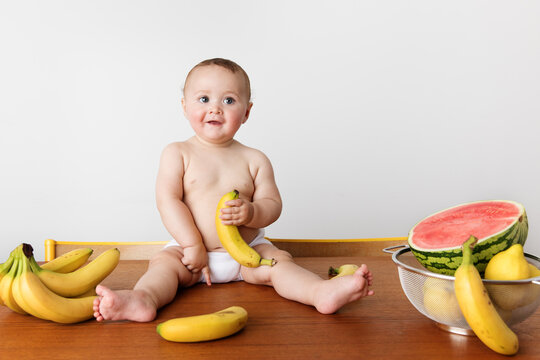 Smiling baby sitting on kitchen table holding banana