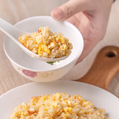 Eating Chinese fried rice in white plate on bright wooden table background.