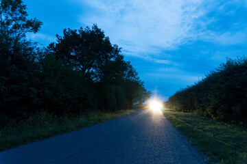A long straight road, With car headlights in the distance. On a summers evening. UK.