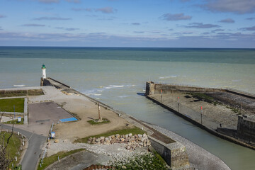 Seawall and pebble beach, lighthouse at entrance to Saint-Valery-en-Caux harbor....