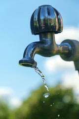 Pouring fresh water  from the metal tap with blurred nature and blue cloudy sky background, selective focus