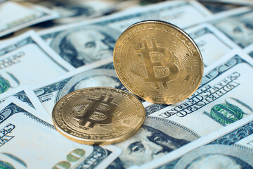 The bitcoin cryptocurrency coin stands on its own end, the second one lies on one hundred dollar bills