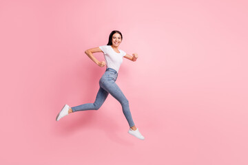 Full size profile photo of optimistic brunette lady jump run wear t-shirt jeans sneakers isolated on pastel pink color background