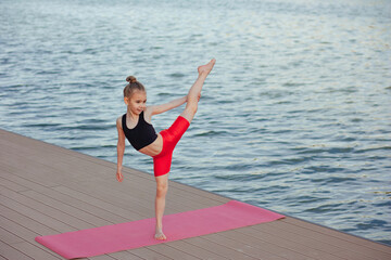 Beautiful young slim girl doing yoga or gymnastic exercise by the lake. Healthy lifestyle. children's sports concept.