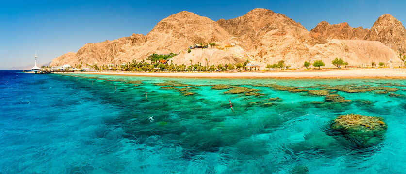 Panoramic view on beautiful coral reefs of the Red Sea, sandy beaches, tourist resort bungalows and mountains near Eilat, Israel