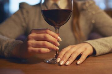 Hand of a young beautiful woman holding a glass of wine indoors of a stylish wine restaurant