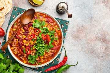 Mexican black bean soup with minced meat, tomato, cilantro, avocado and vegetables stew on a light grey slate, stone or concrete background. Traditional Mexican dish. Top view with copy space.