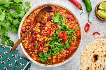 Mexican black bean soup with minced meat, tomato, cilantro, avocado and vegetables stew on a light grey slate, stone or concrete background. Traditional Mexican dish. Top view with copy space.