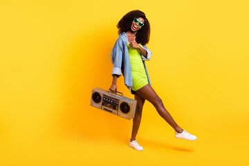 Full length body size view of beautiful trendy cheerful girl demonstraing copy space carrying player isolated over bright yellow color background