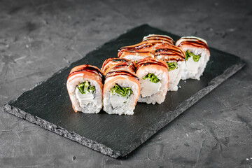 appetizing sushi roll with cheese salad and jamon on a black stone plate