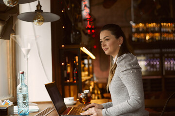 Young beautiful woman girl working behind a laptop looks out the window. She is in a good mood from the message she read. Concept freelance work.