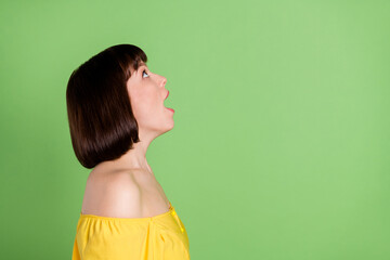Profile side photo of shocked young positive woman look up empty space information isolated on green color background