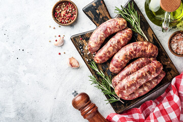 Raw sausages or bratwurst on cutting board with spices and ingredients for cooking. Top view with copy space on light grey stone table.
