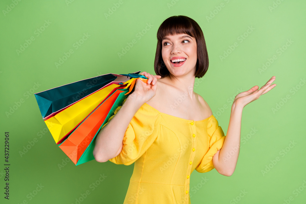 Sticker Photo of attractive dreamy happy young woman look empty space hold hands bags isolated on green color background