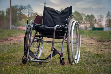 Empty wheelchair standing on grass in hospital park waiting for patient services. Invalid chair for disabled people parked outdoor in nature. Handicap accessible symbol. Health care medical concept