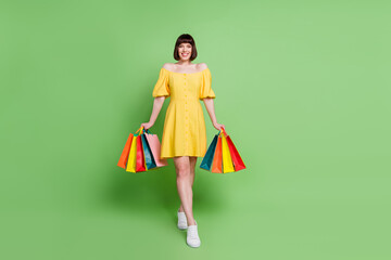 Full body photo of attractive positive young woman hold hands shopping bags walk isolated on green color background