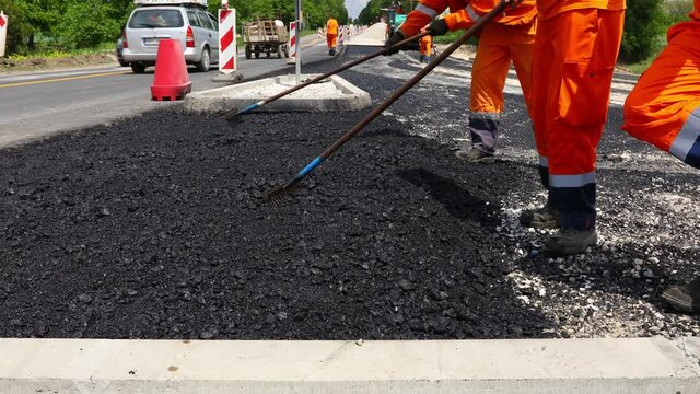 Few workers are using rake to level, set up layer of fresh tarmac to right measures, pouring hot asphalt.