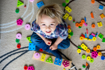 Little blonde toddler child,  boy playing with wooden toys developing and learning