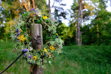 Colorful wreath of flowers, bent and twigs, hung on a wooden pole during the summer solstice...