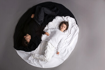 Two children, dressed in black and white, lying on the floor in Yin -Yang circle - obrazy, fototapety, plakaty